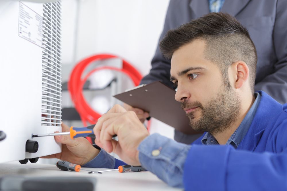 a Technician in Blue Overalls Uses a Screwdriver on a White Machine — Don Hall Air Conditioning & Electrical in Smithfield, QLD