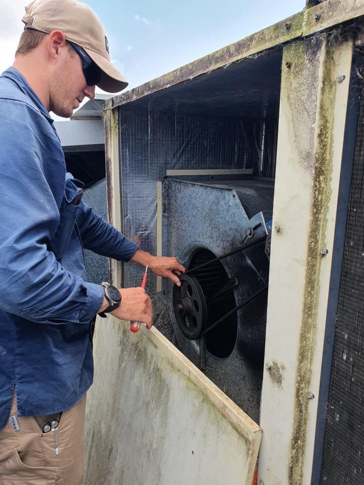Man in a Cap Working on Hvac Unit, Holding a Tool; Outdoors — Don Hall Air Conditioning & Electrical in Smithfield, QLD