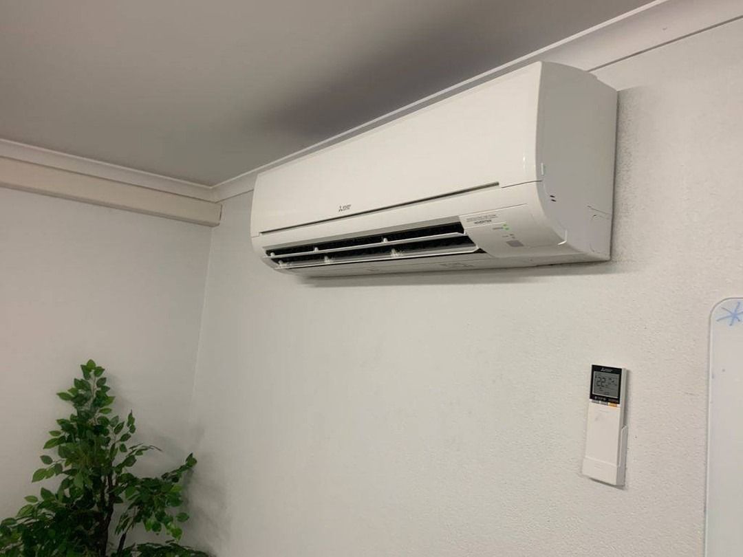 White air conditioner above a window looking into a small garden, with a clock to the left— Don Hall Air Conditioning & Electrical in Smithfield, QLD
