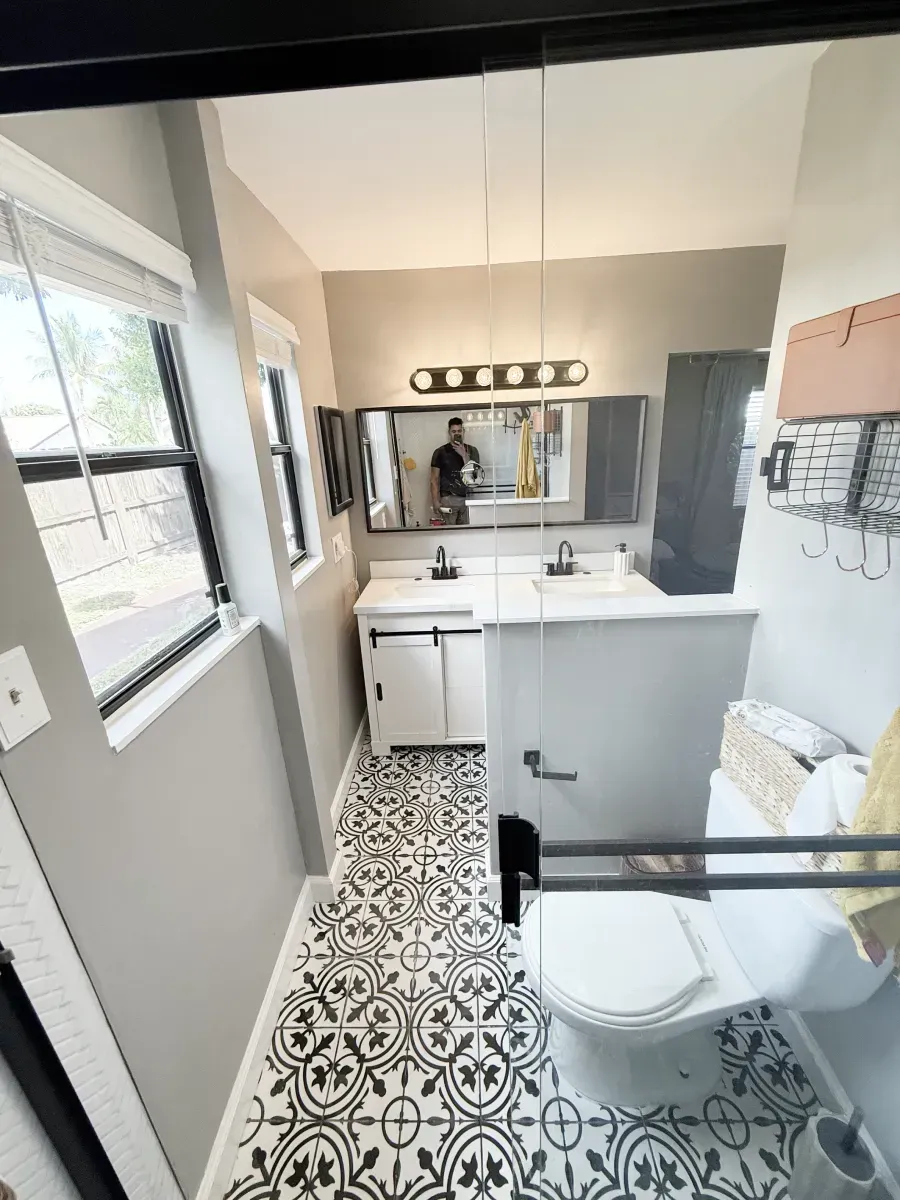 A small bathroom with patterned black-and-white tile flooring, a white vanity, a large mirror, and a white toilet.