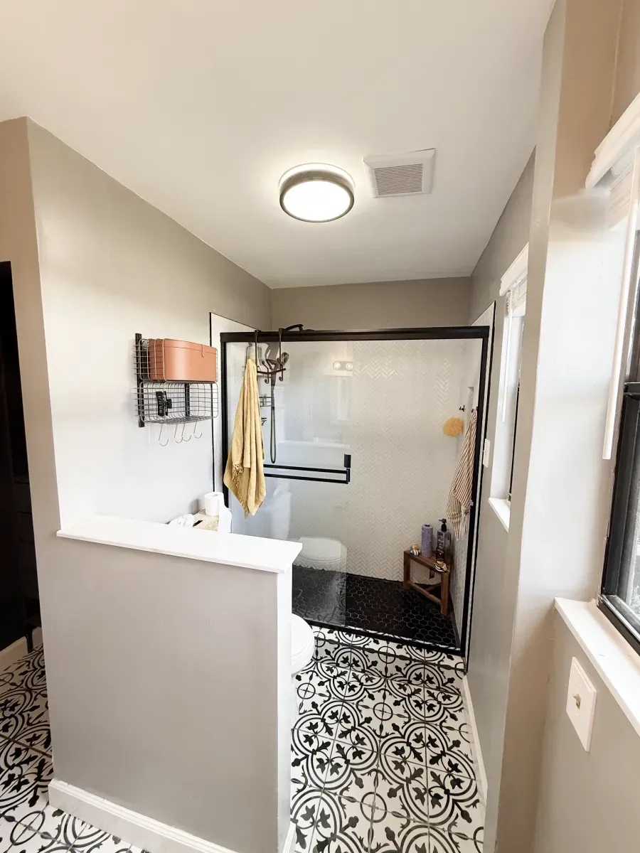 A bathroom with a half-wall partition, black-and-white patterned floor tiles, a glass shower stall, and a neutral color.