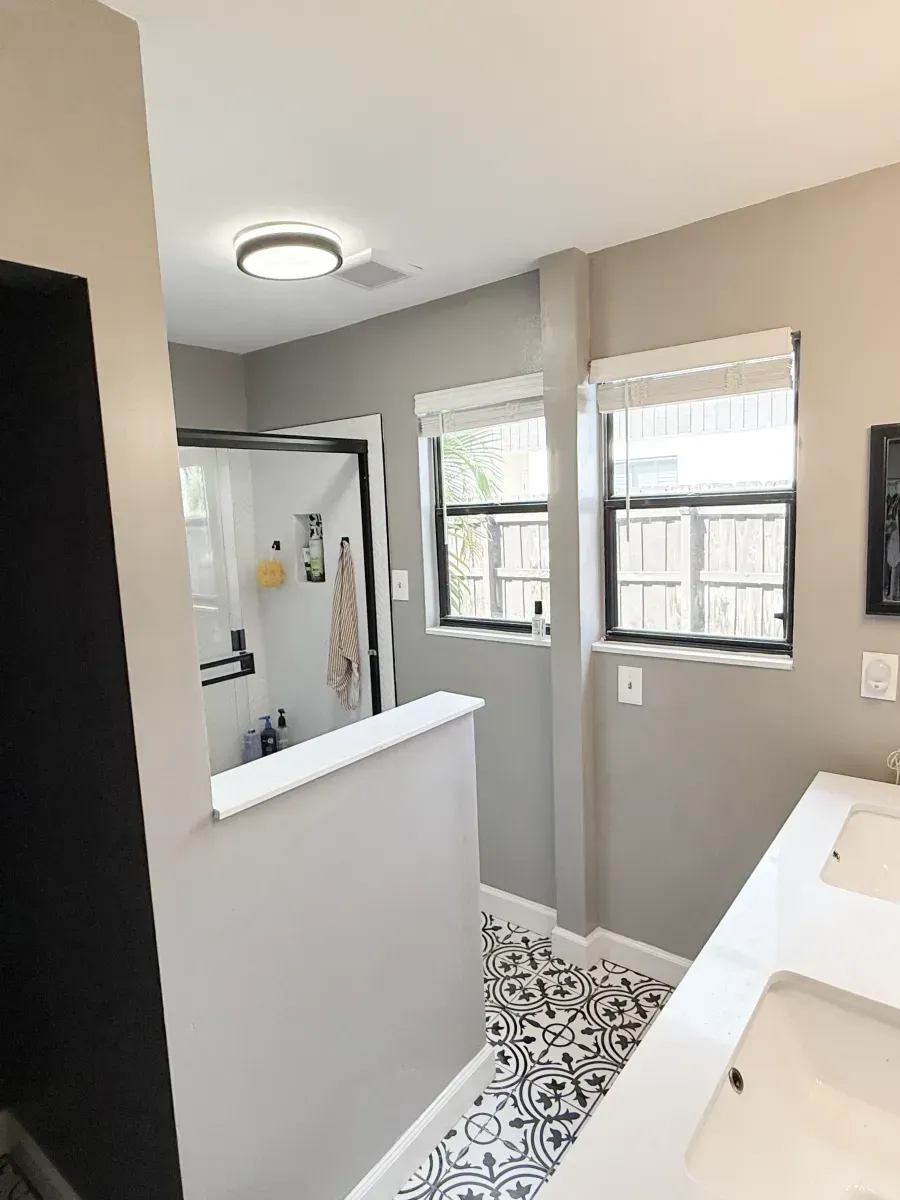 Modern bathroom featuring a double vanity, patterned black-and-white floor tiles, and a walk-in shower behind a low wall.