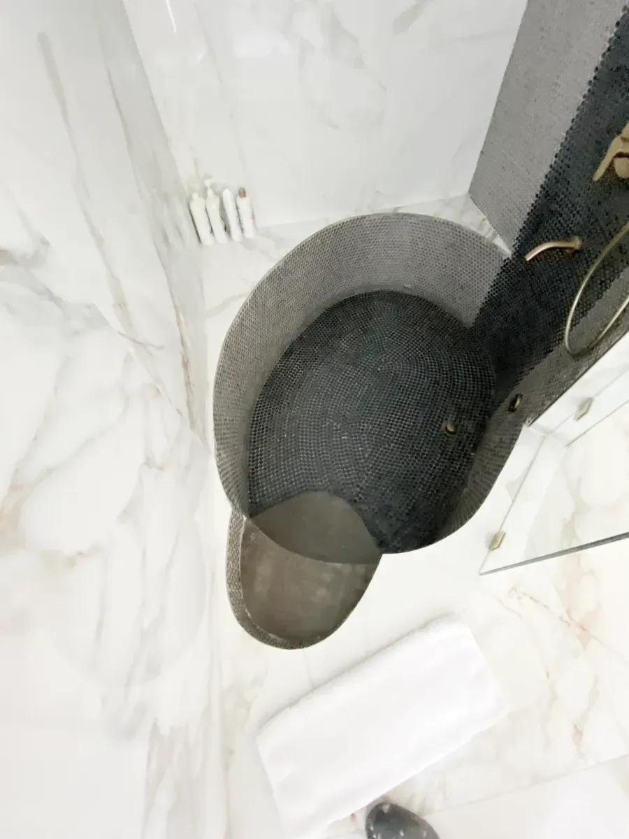 A dark, circular bath mat rests on a white, marble-patterned tile floor next to a white towel.