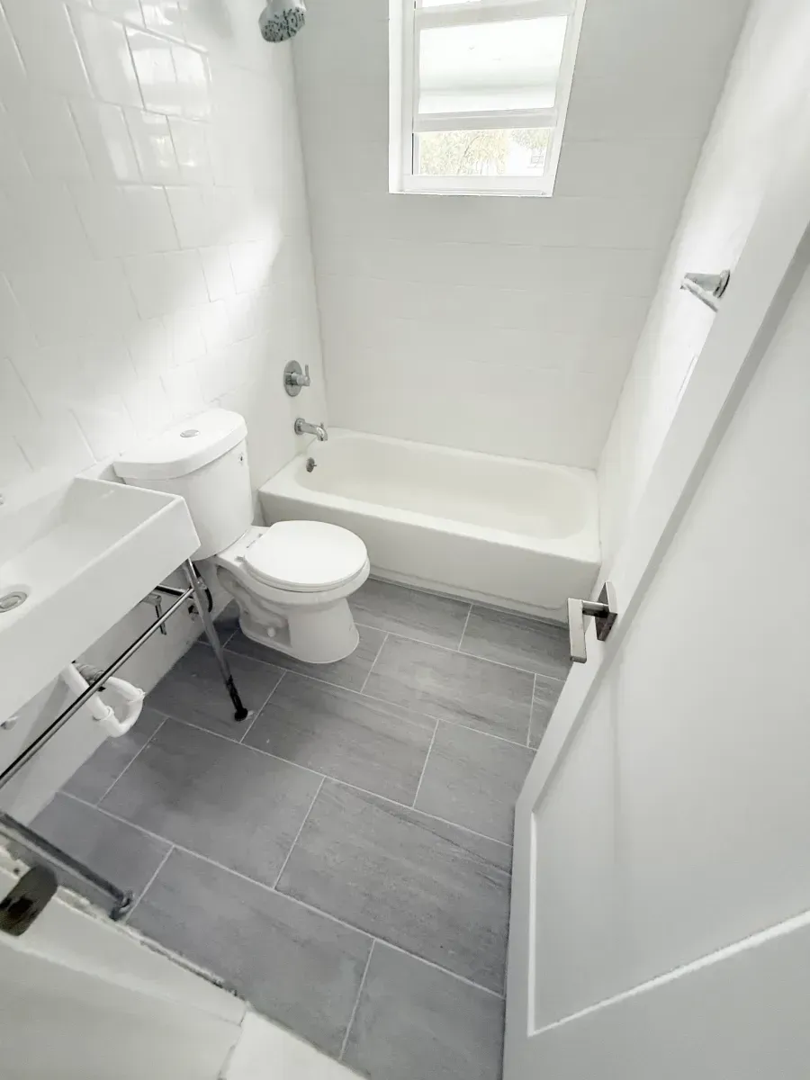 A modern bathroom with a white sink, white toilet, and white bathtub, featuring grey tile flooring.