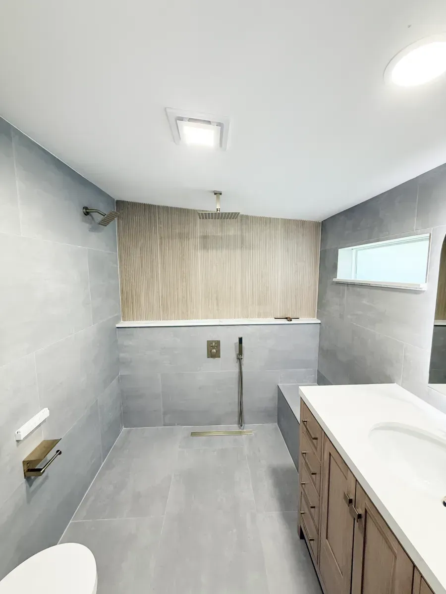 A modern bathroom with grey tiled walls, a wood-paneled shower area, a walk-in shower with a glass door, and a wood vanity.