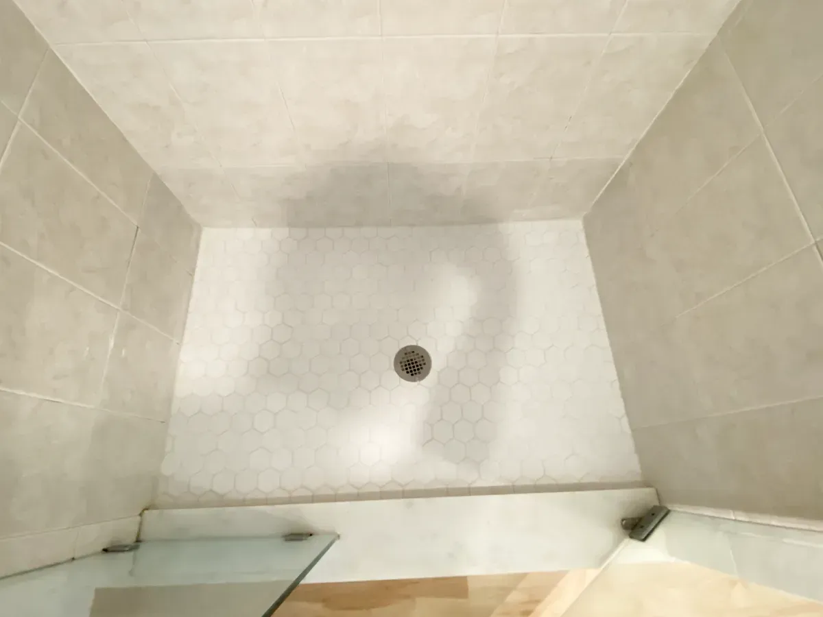 A view looking down into a tiled shower stall with a center drain and light-colored walls.