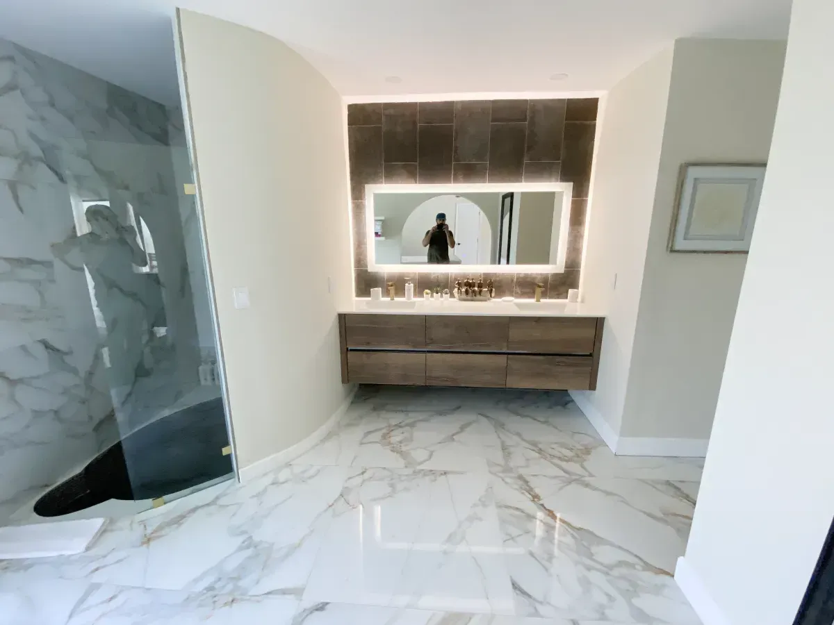 Modern bathroom featuring a wood floating vanity, backlit mirror, marble flooring, and a glass-enclosed shower.