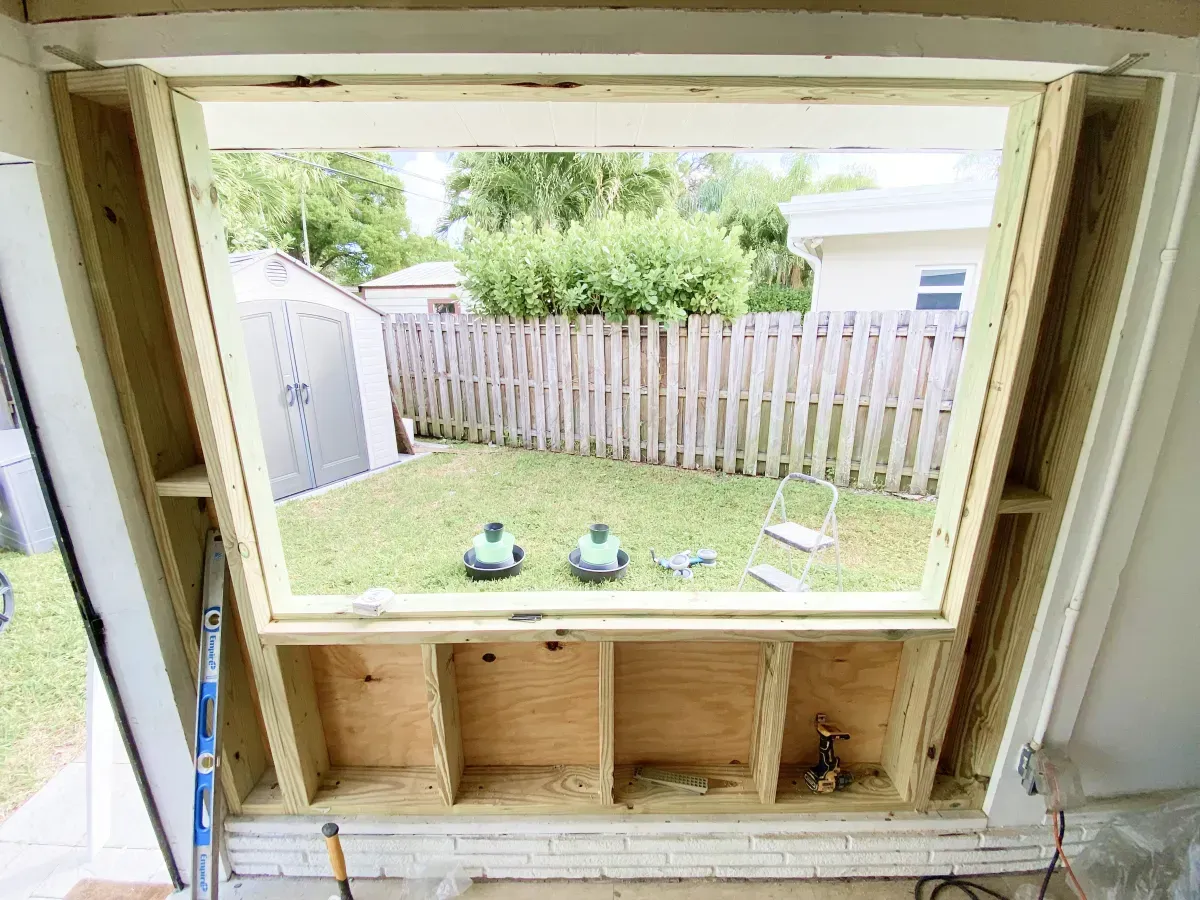 A wooden window frame installed in a wall, overlooking a grassy backyard with a fence.