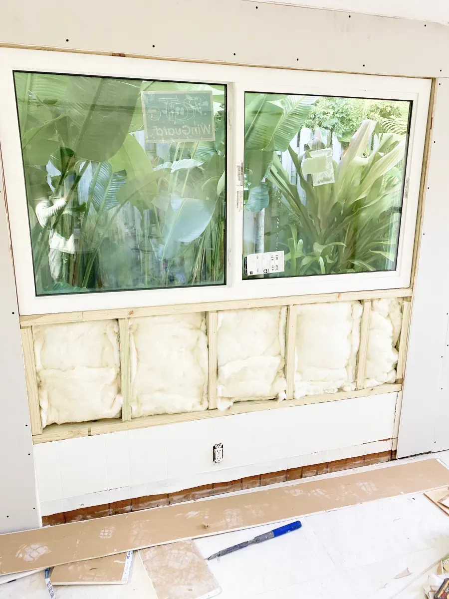 A window installation in a wall with exposed wooden framing, fiberglass insulation, and unfinished drywall.