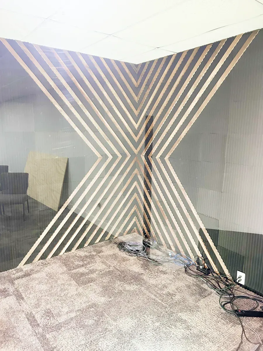 A corner wall featuring a modern, geometric wood slat pattern creating an X design against a plain, light-colored background.