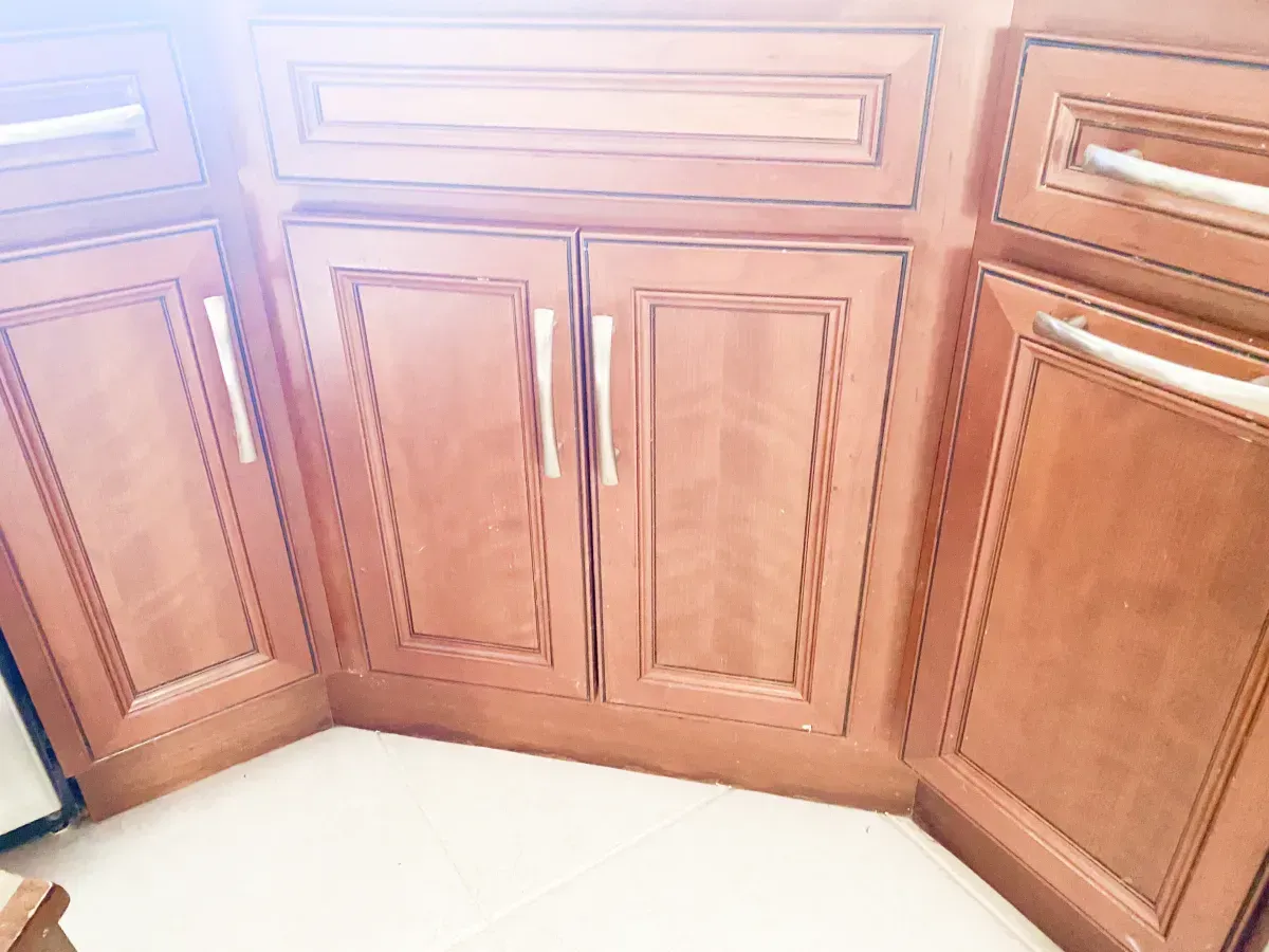 Corner kitchen cabinets featuring medium-brown wood doors with decorative molding and brushed silver hardware.