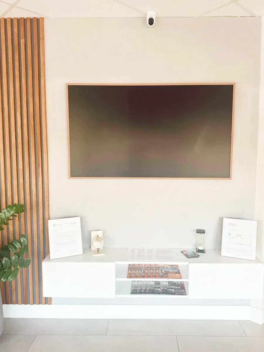 A television mounted on a beige wall with a wooden slat accent panel, featuring a white floating media console below.