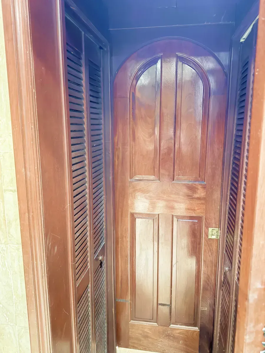 An arched wooden door centered between two louvered wooden closet doors in a narrow hallway.