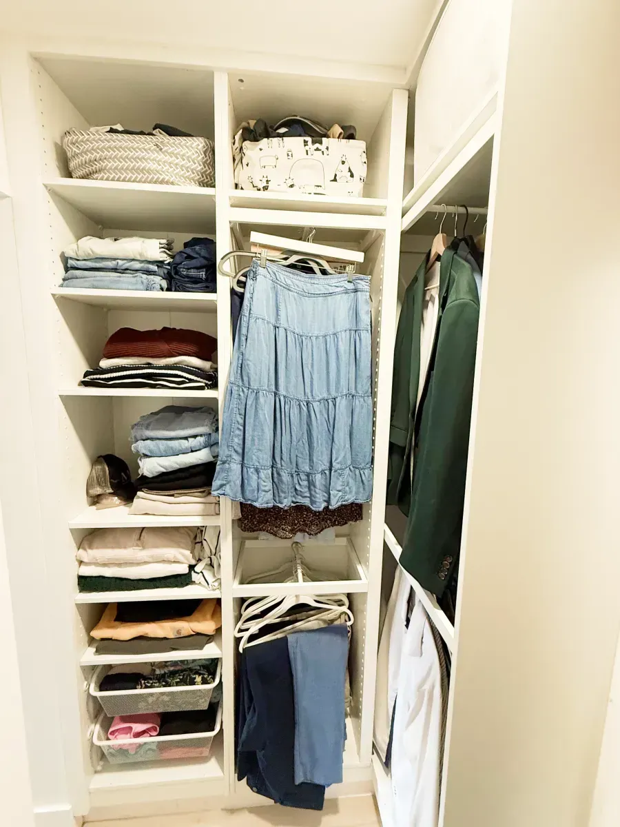 An organized white closet with shelves holding folded clothes, baskets, and hanging garments on racks.