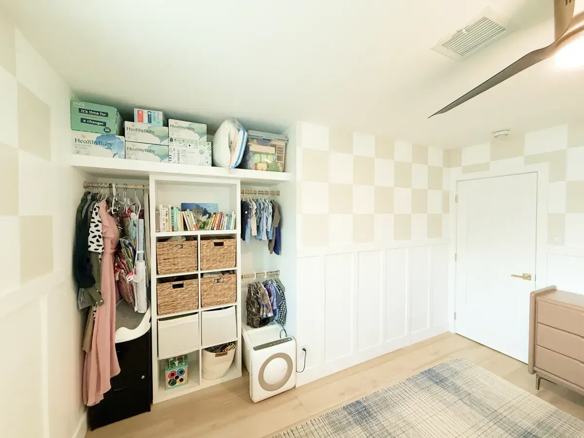 A closet with clothing racks, a shelving unit holding wicker baskets and bins, and a white door in a checkered-wall room.