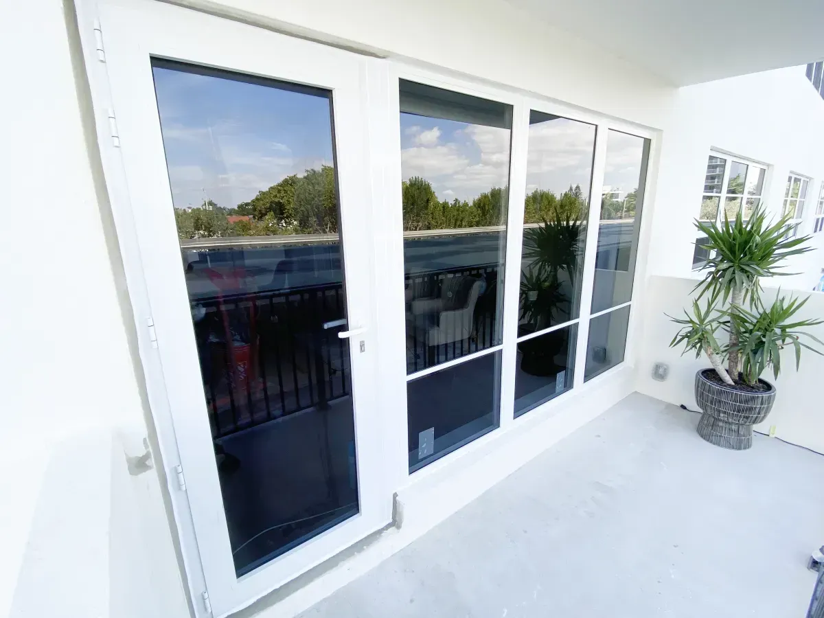 A white balcony door and large glass panels on a bright, modern patio with a potted plant on a grey floor.