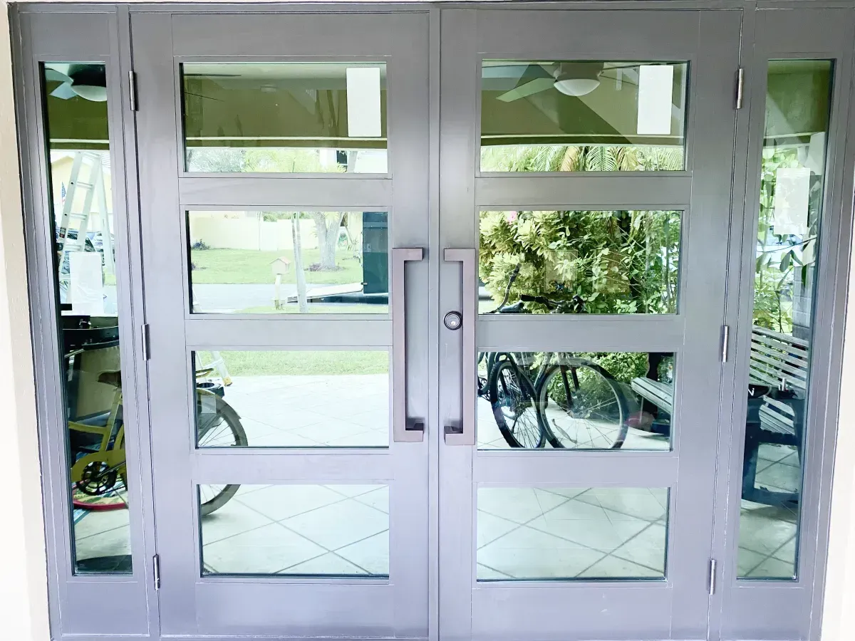 White double doors with four glass panels each and side windows, viewed from inside looking out onto a tiled porch.