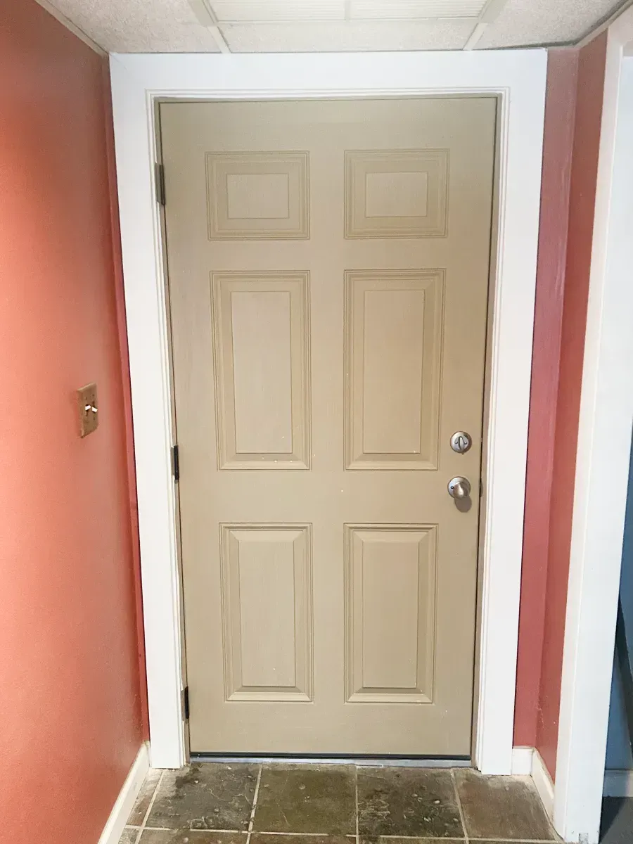 A tan six-panel door framed in white against reddish-orange walls, set above a tiled floor.