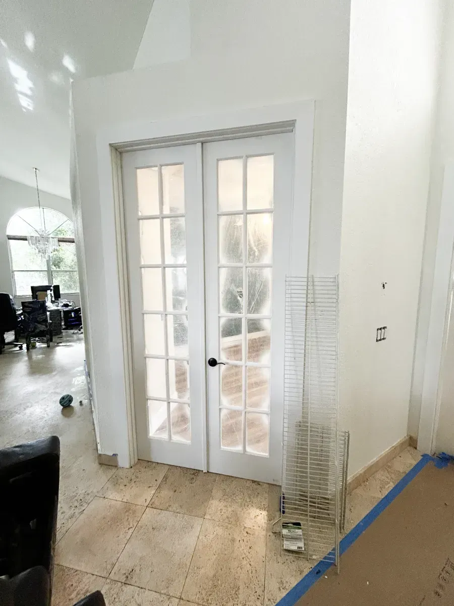 White French doors with glass panes installed in a room with light-colored tile floors and unfinished construction areas.