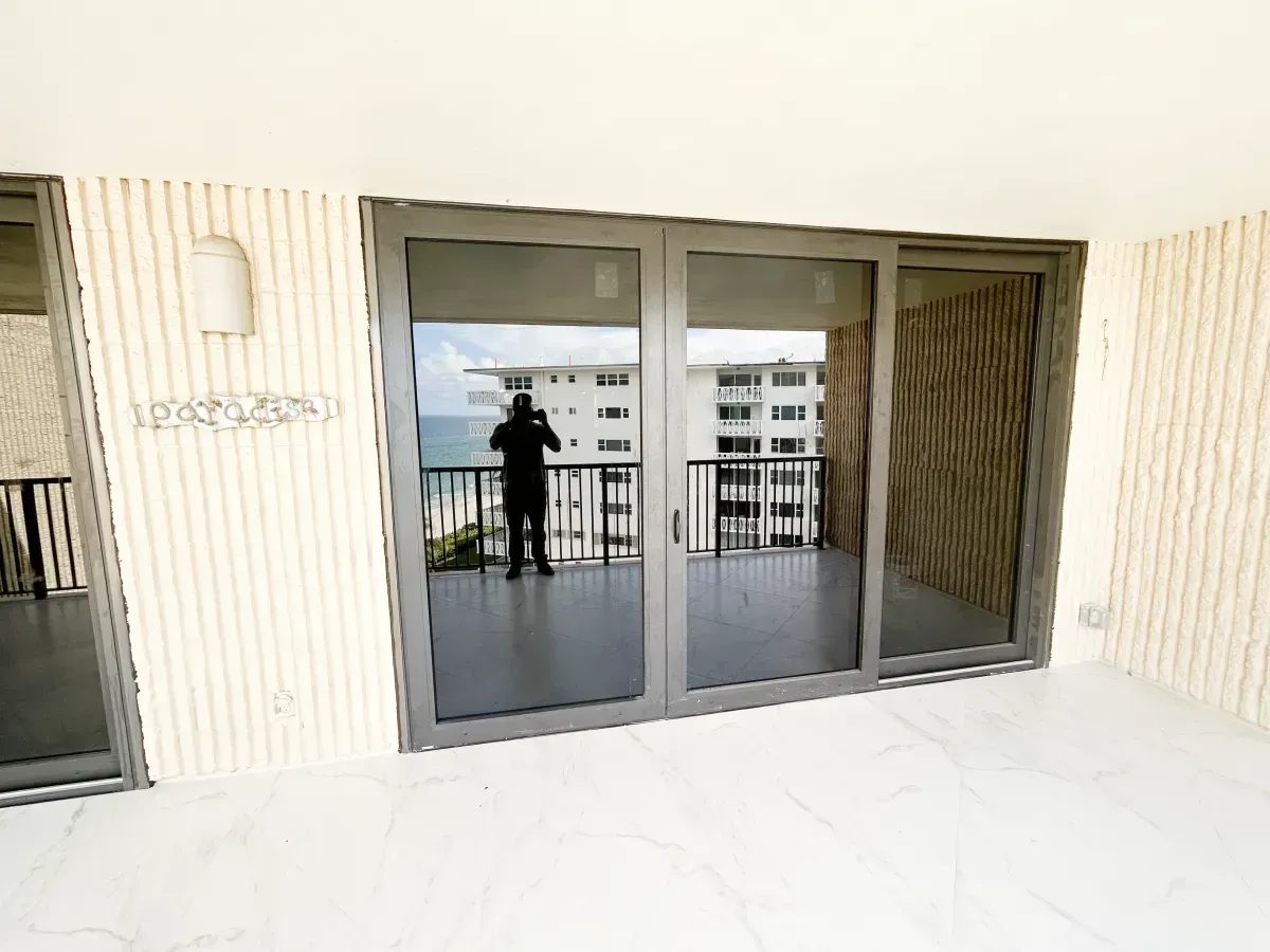 An interior room with white tiled floors and sliding glass doors leading to a balcony overlooking the ocean.