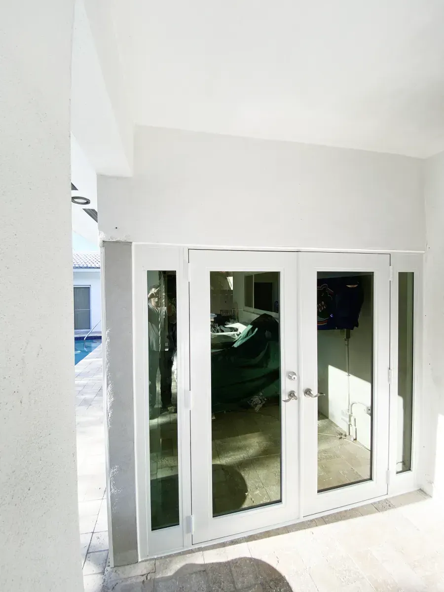 White French doors with side panels open onto a bright patio area, with a pool visible in the background.
