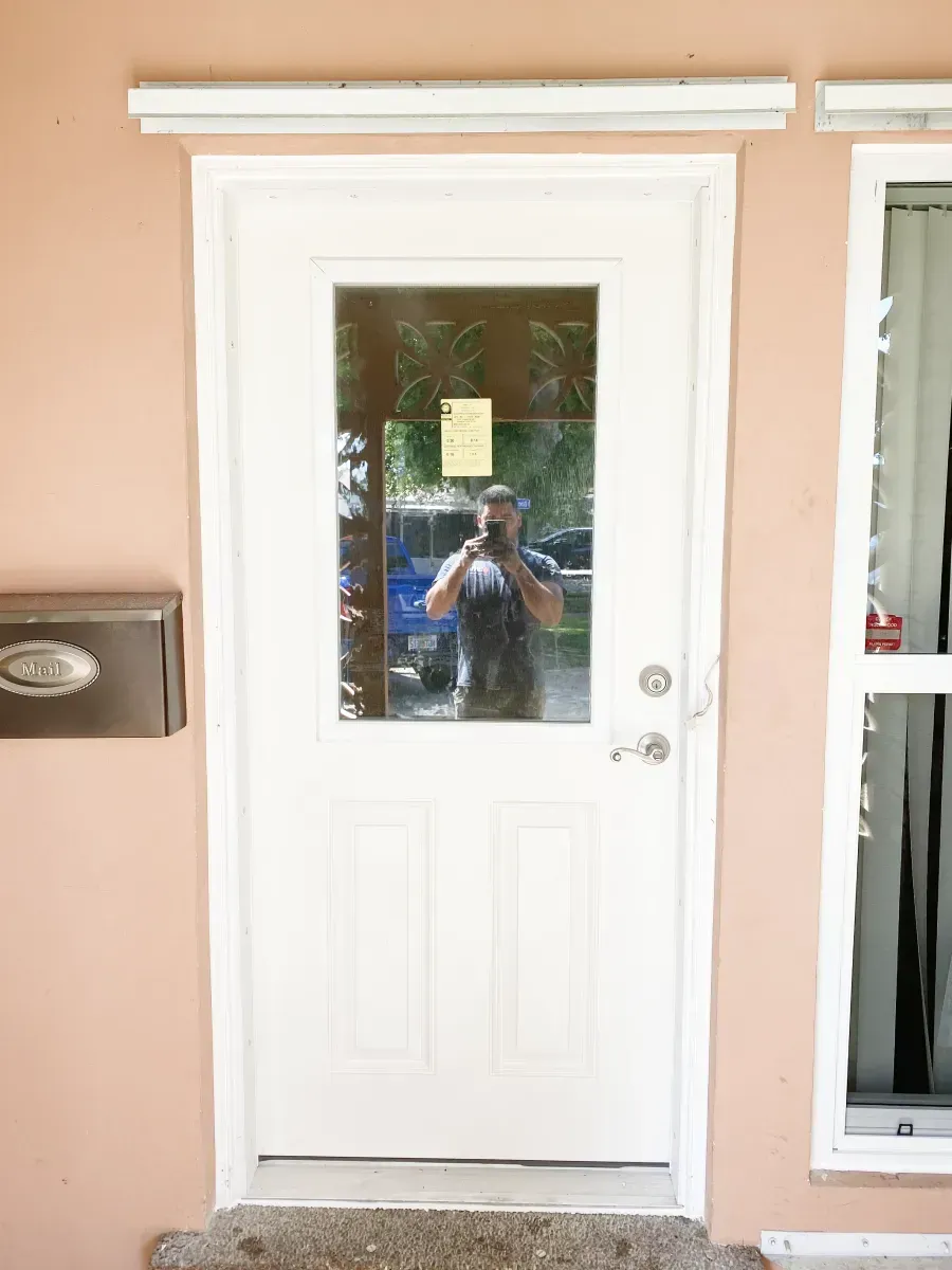 A white exterior door with a glass window panel is set into a peach-colored wall next to a silver mailbox.