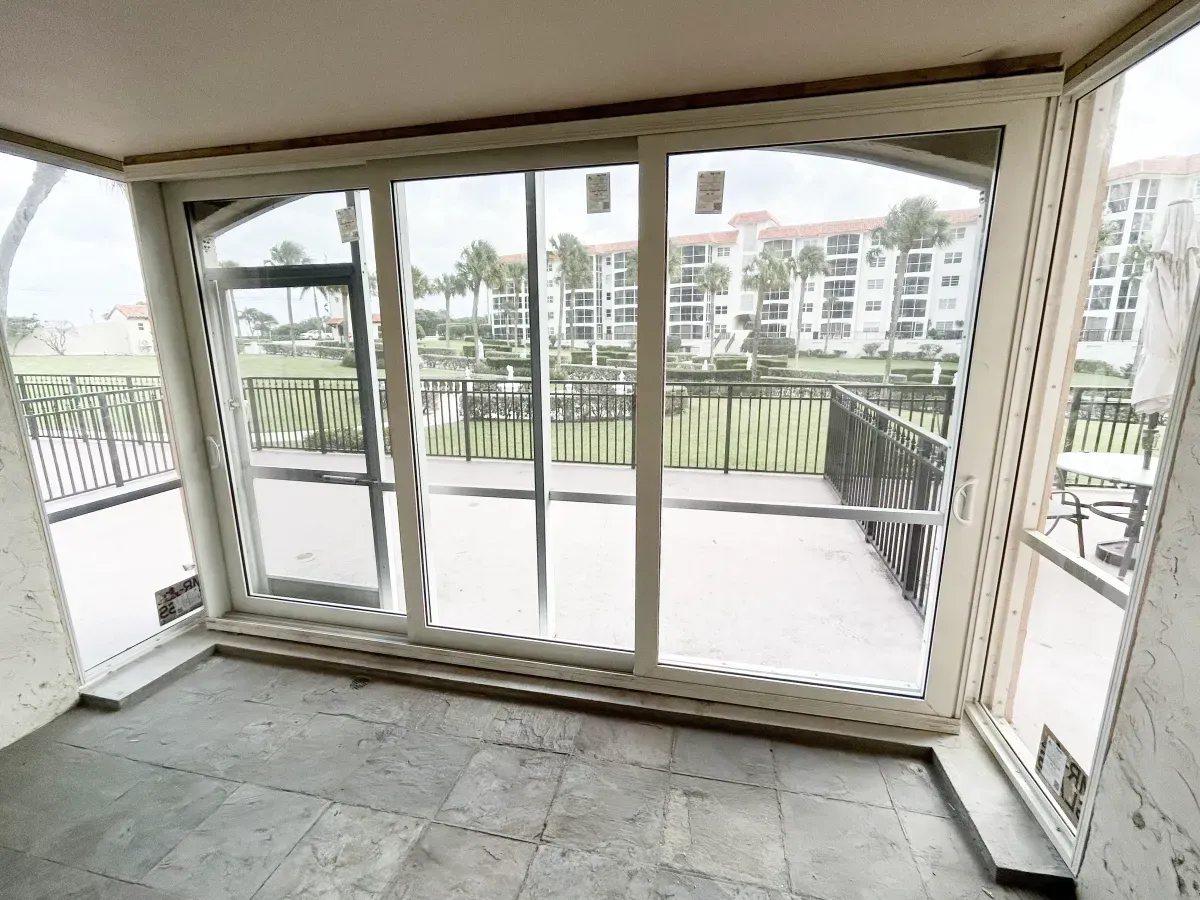 A sunroom with stone flooring featuring large sliding glass doors overlooking an outdoor balcony and complex building.