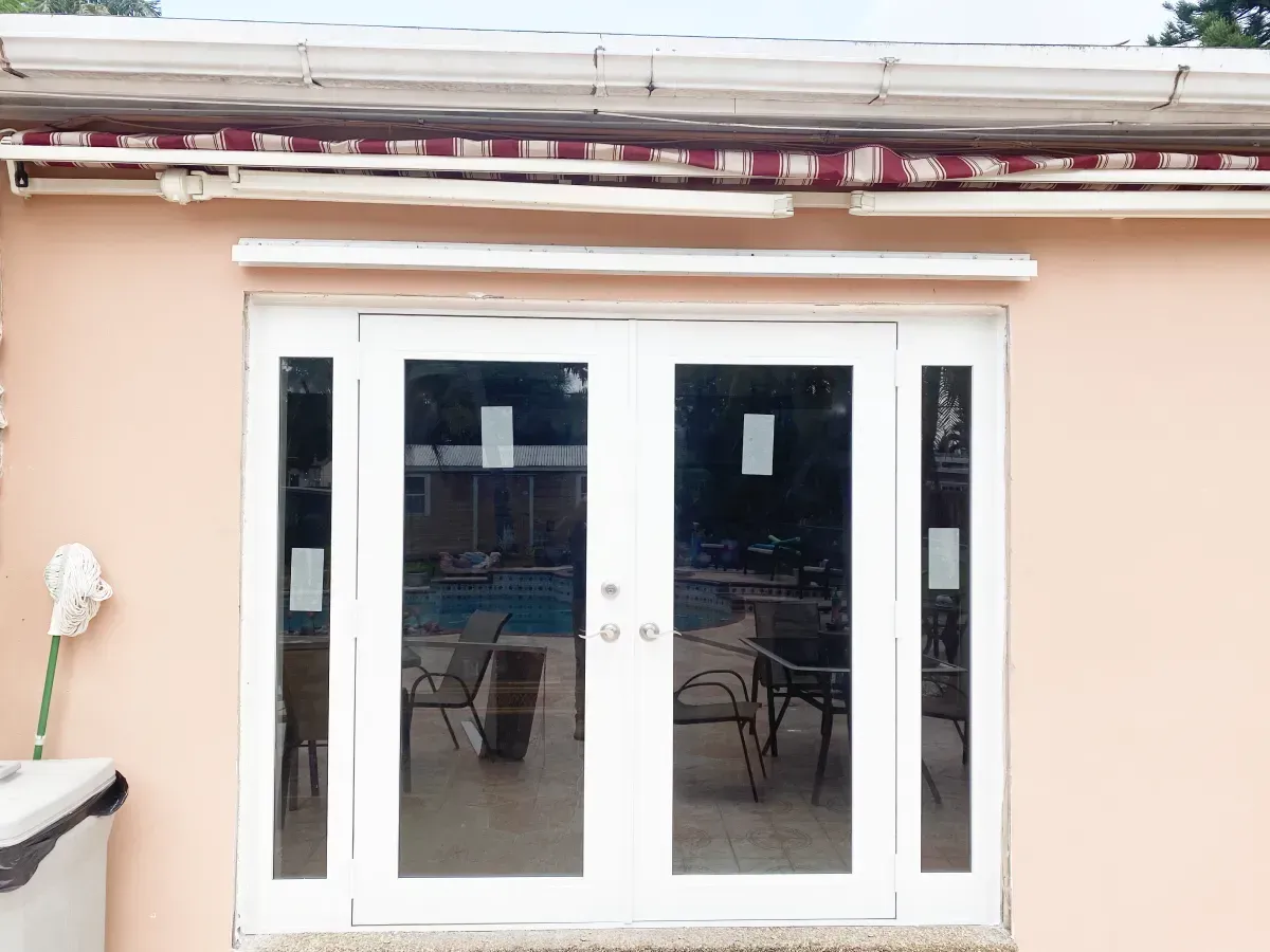 Exterior view of white French doors with sidelights set into a peach-colored wall, topped by a red and white striped awning.