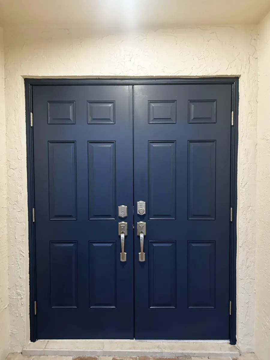 A set of double entry doors painted dark navy blue, featuring six panels each and silver handle sets with deadbolts.