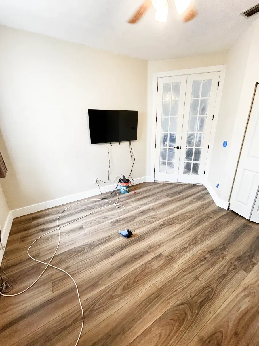 A small room with wood-look flooring, a wall-mounted television with exposed wires, and glass-paneled double doors.