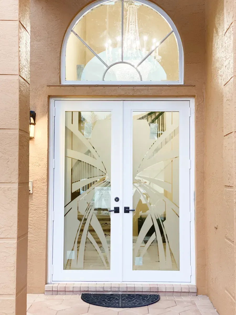 White double front doors with etched glass designs, topped by an arched window in a tan stucco entryway.