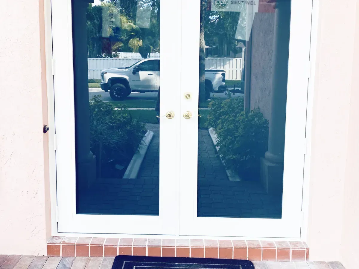White double doors with glass panels reflecting a driveway and truck, set in a light-colored wall with a brick threshold.
