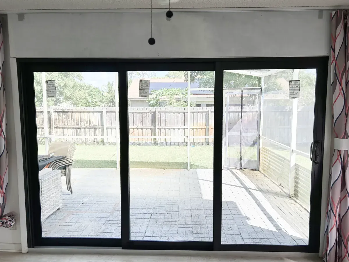 Large black-framed sliding glass doors look out onto a backyard patio with a wooden fence and covered enclosure.
