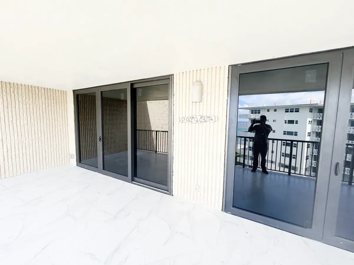 A balcony with white tiled flooring, large glass sliding doors, and vertical wood-paneled walls.