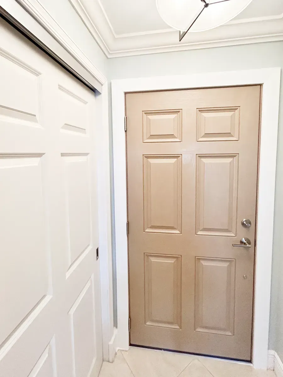 A light-colored six-panel door with silver hardware stands next to a white sliding closet door in a tiled entryway.