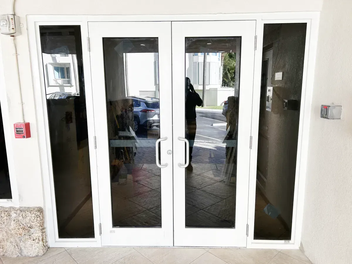 A pair of white-framed glass double doors with side panels and silver handles at a building entrance.
