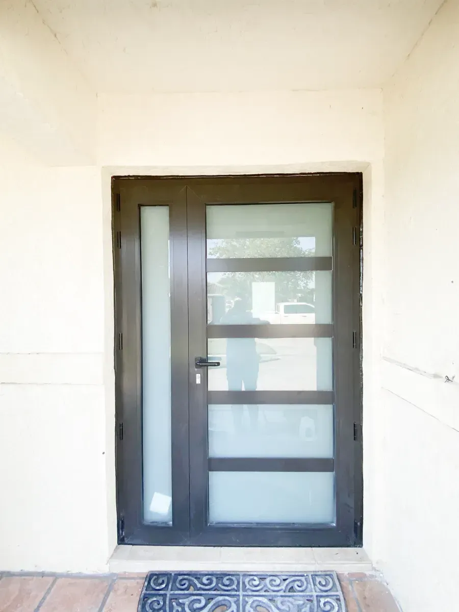 A dark-framed front door with a vertical frosted glass pane next to four horizontal frosted glass panels.