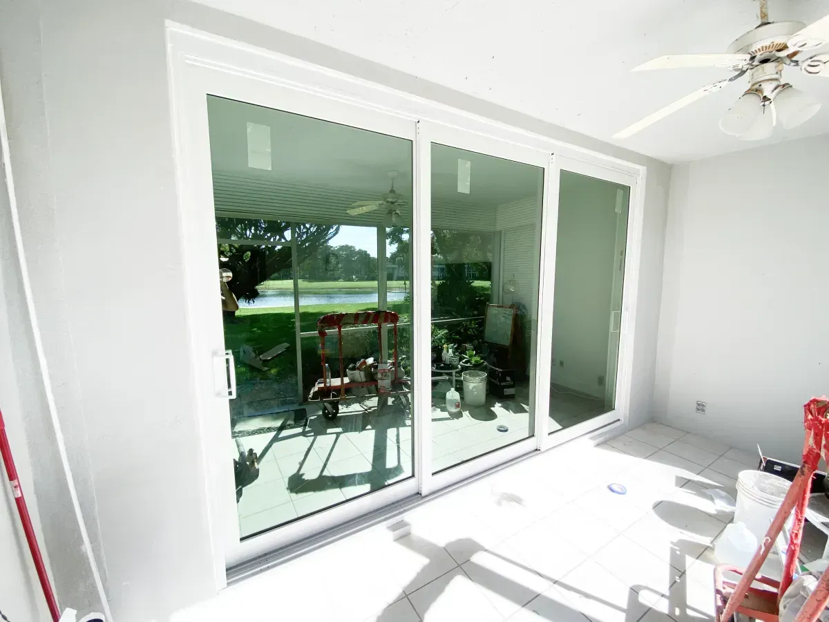 Bright, white-walled room with a sliding glass door looking out onto a green backyard and a ceiling fan overhead.