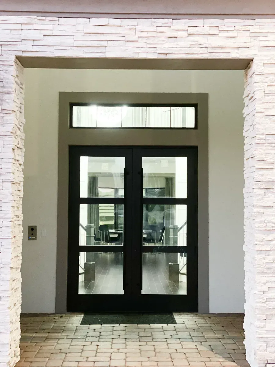 Double doors with glass panes and a transom window, framed by light-colored stacked stone, leading into a bright interior.