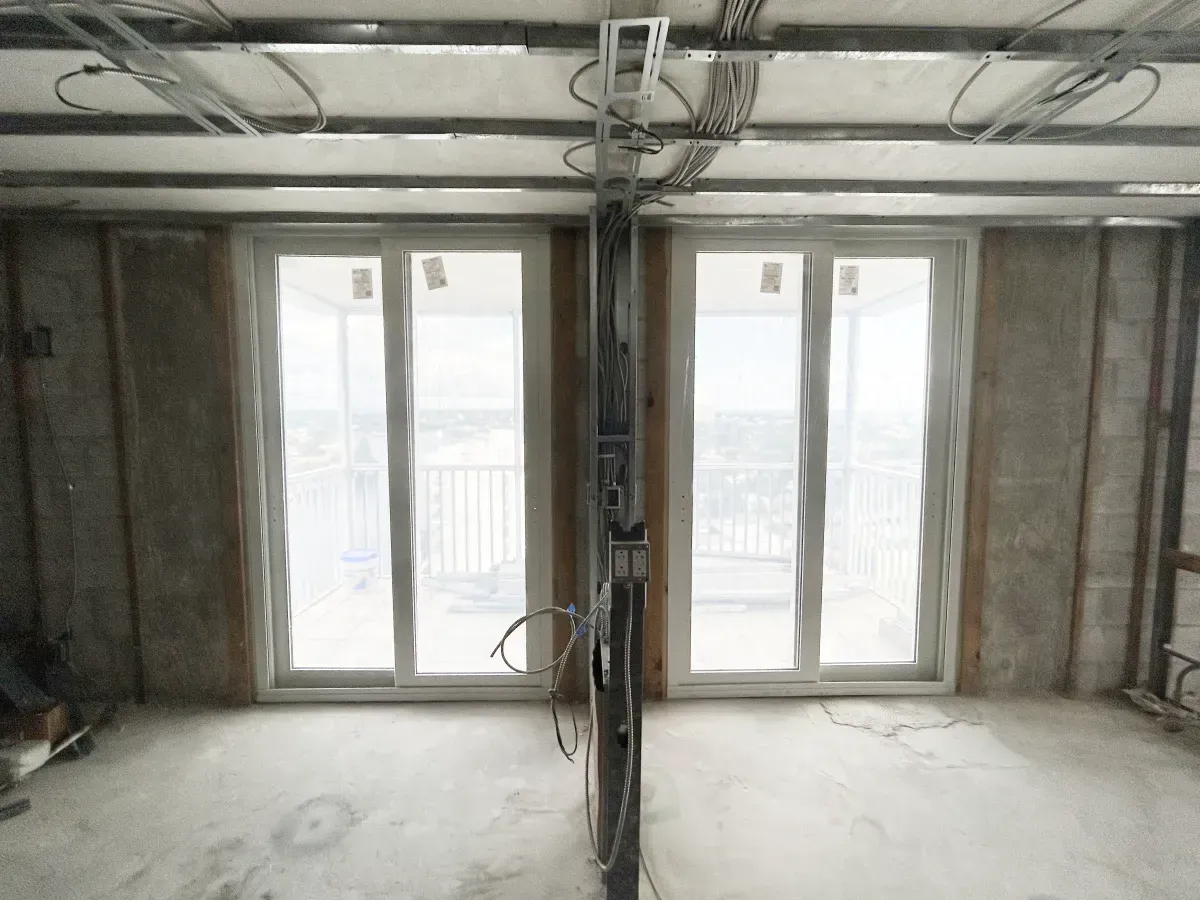 Interior view of a room under construction with concrete walls, metal framing, and two side-by-side sliding glass doors.
