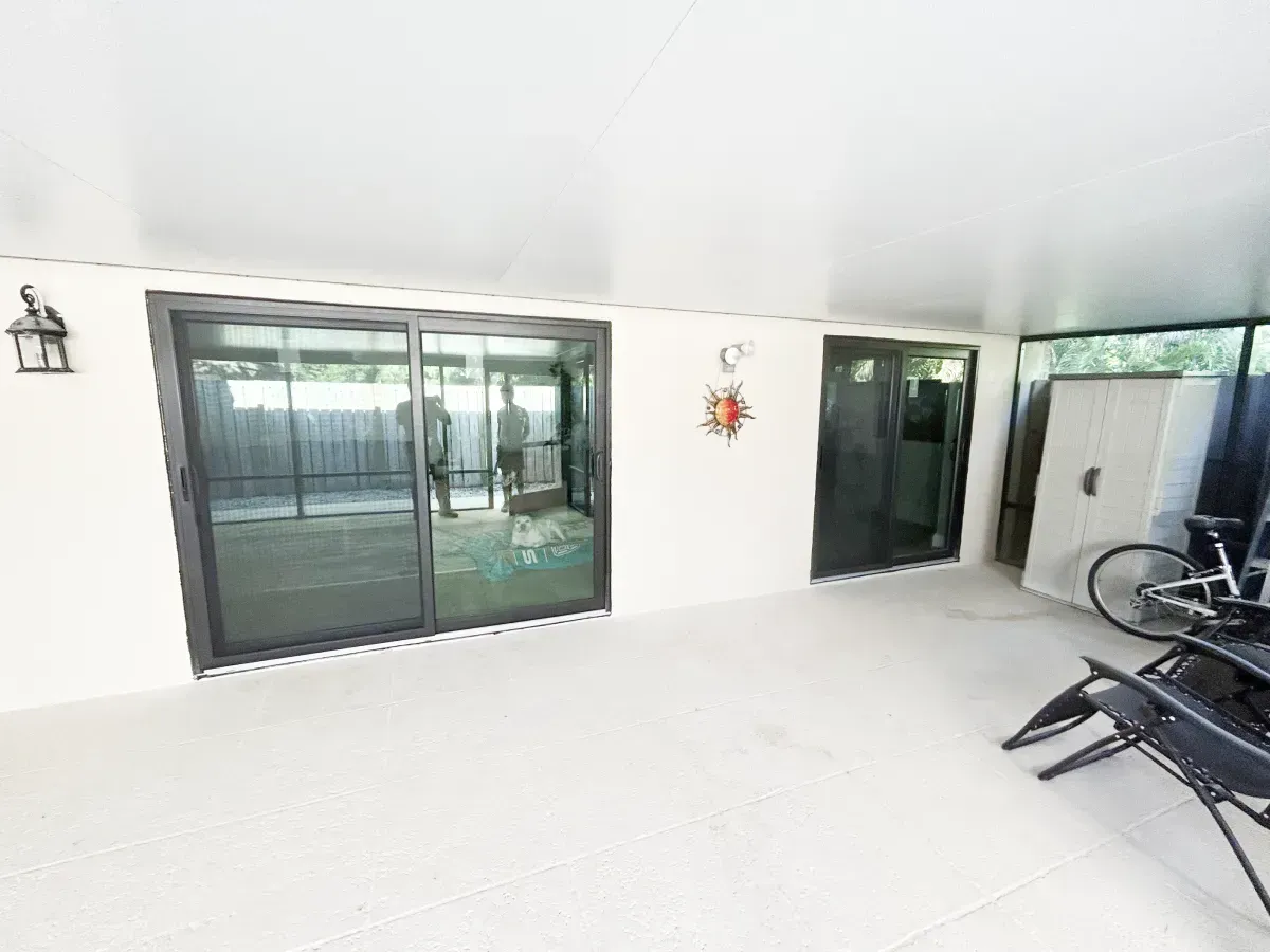 A covered outdoor patio featuring light floors, white walls, two sliding glass doors, and a bicycle parked to the right.