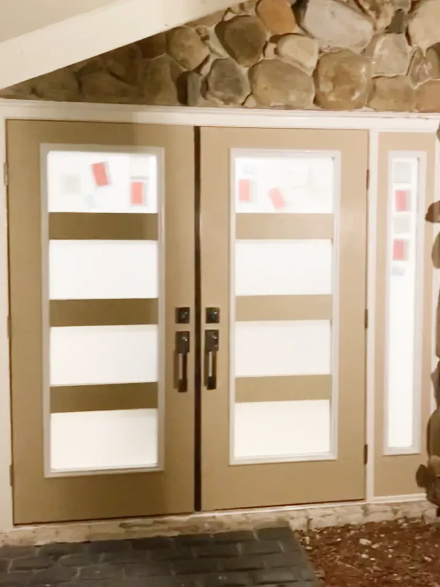 Double doors with four horizontal frosted glass panels each, set against a stone wall with an adjacent sidelight.