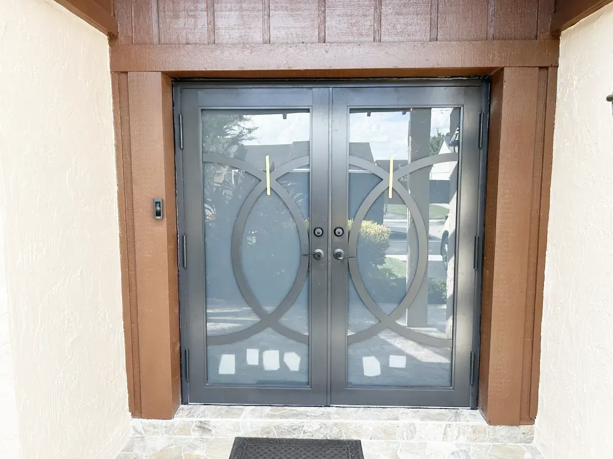 Double doors with a dark metal frame and decorative circular design, set within a brown wood-trimmed entryway.