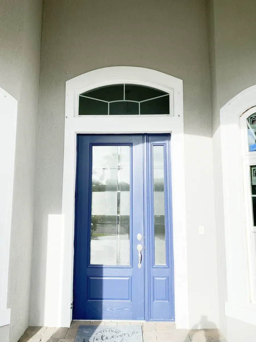A blue front door with a glass panel and a semi-circular transom window set in a light-colored stucco entrance.