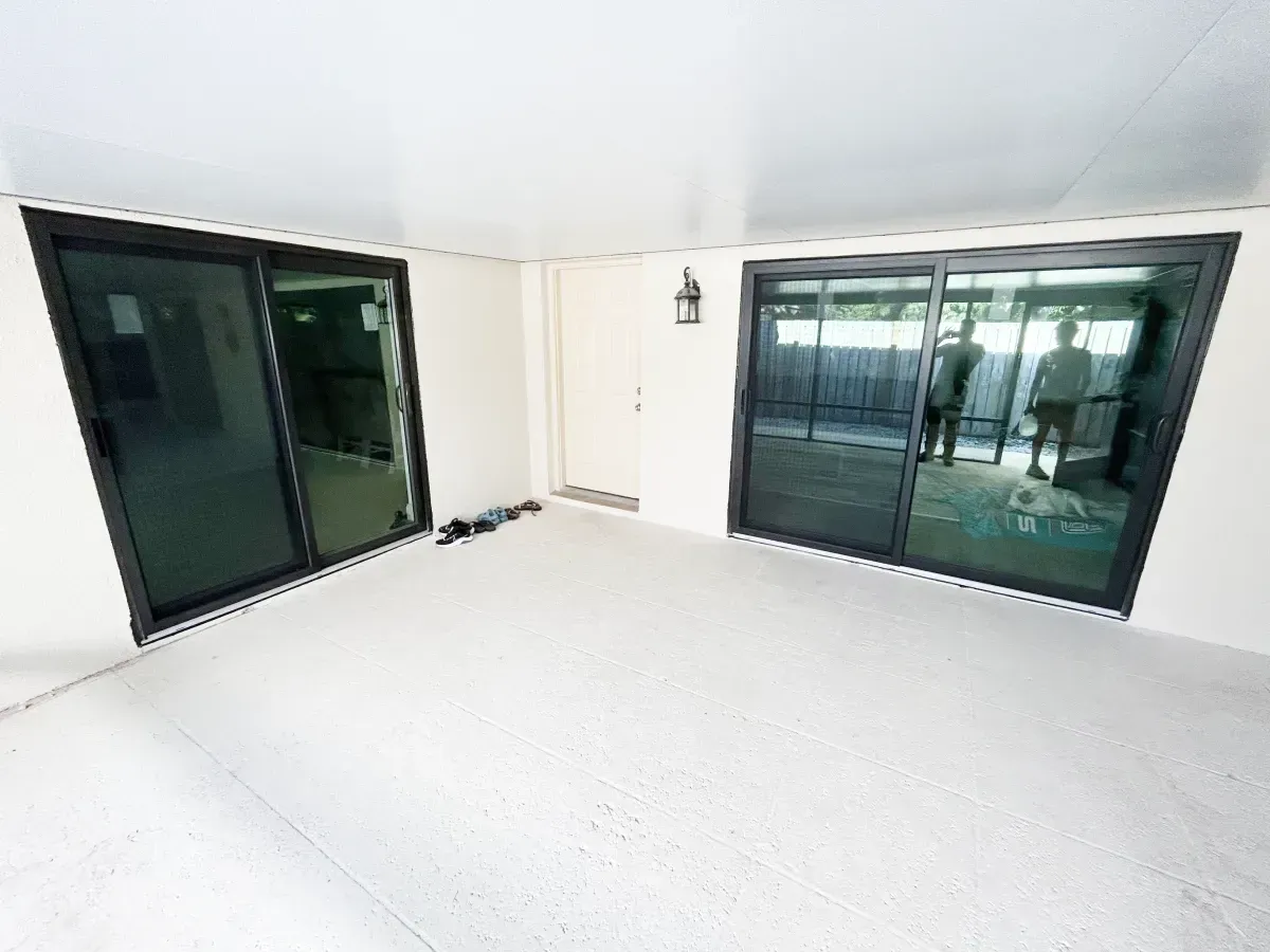 A covered outdoor patio featuring light-colored flooring, white walls, and two large sliding glass doors.