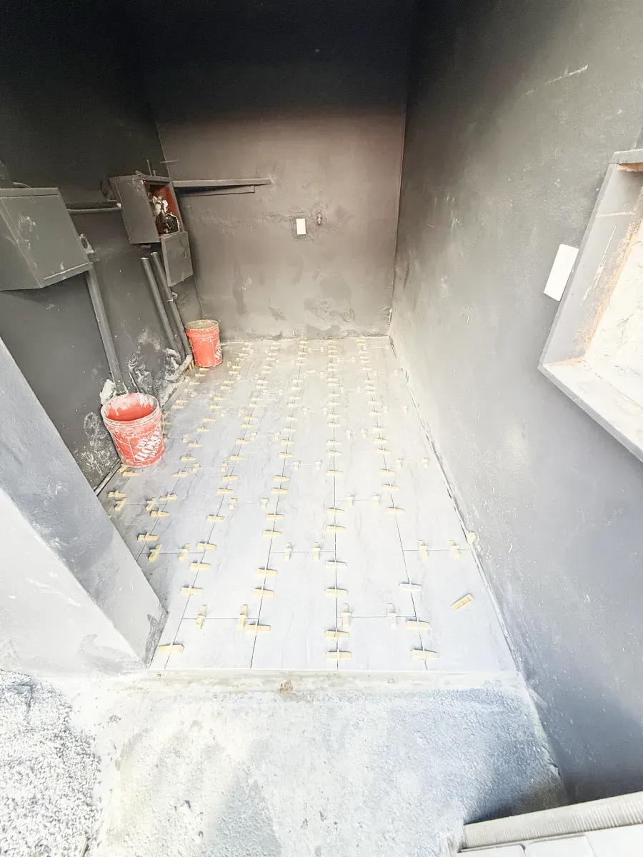A narrow, dark interior space under construction with grey walls and a floor covered in evenly spaced tile spacers.