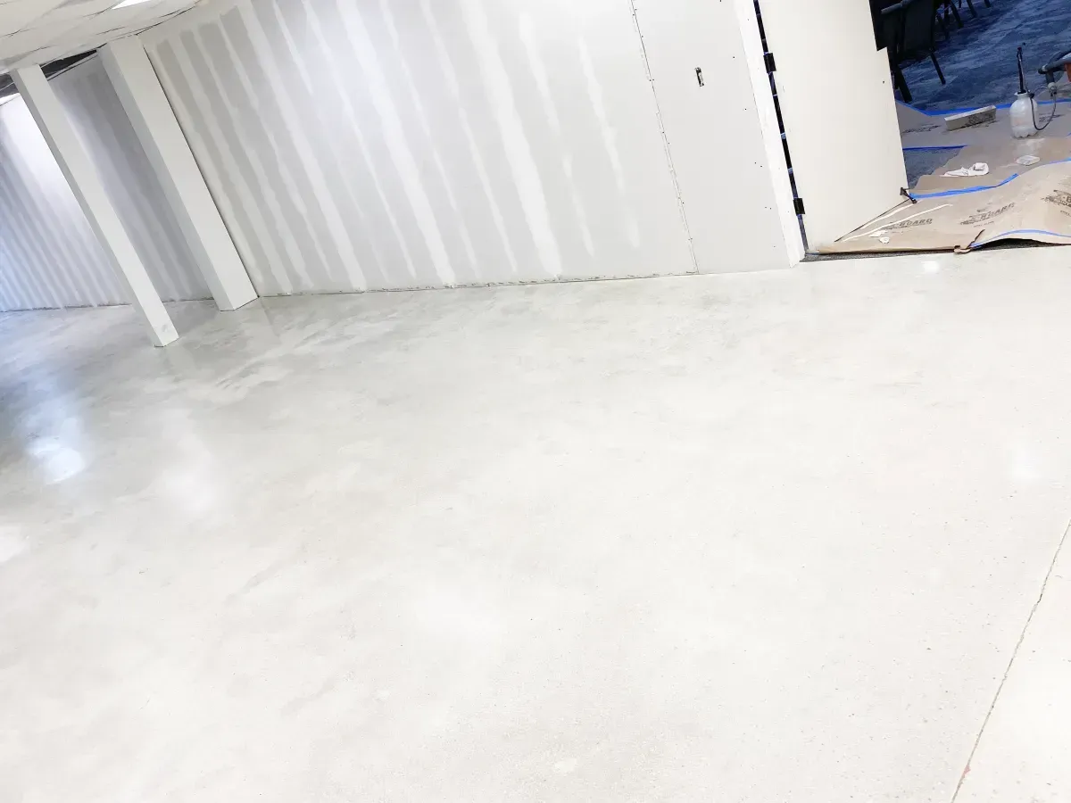 A bright, empty indoor space with polished light gray concrete floors and white unfinished walls under construction.