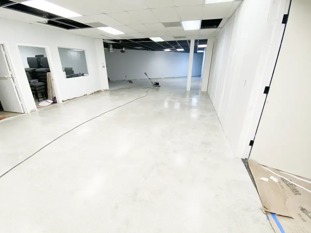 An empty, renovated commercial space with light-colored, polished concrete floors and white walls under drop ceilings.