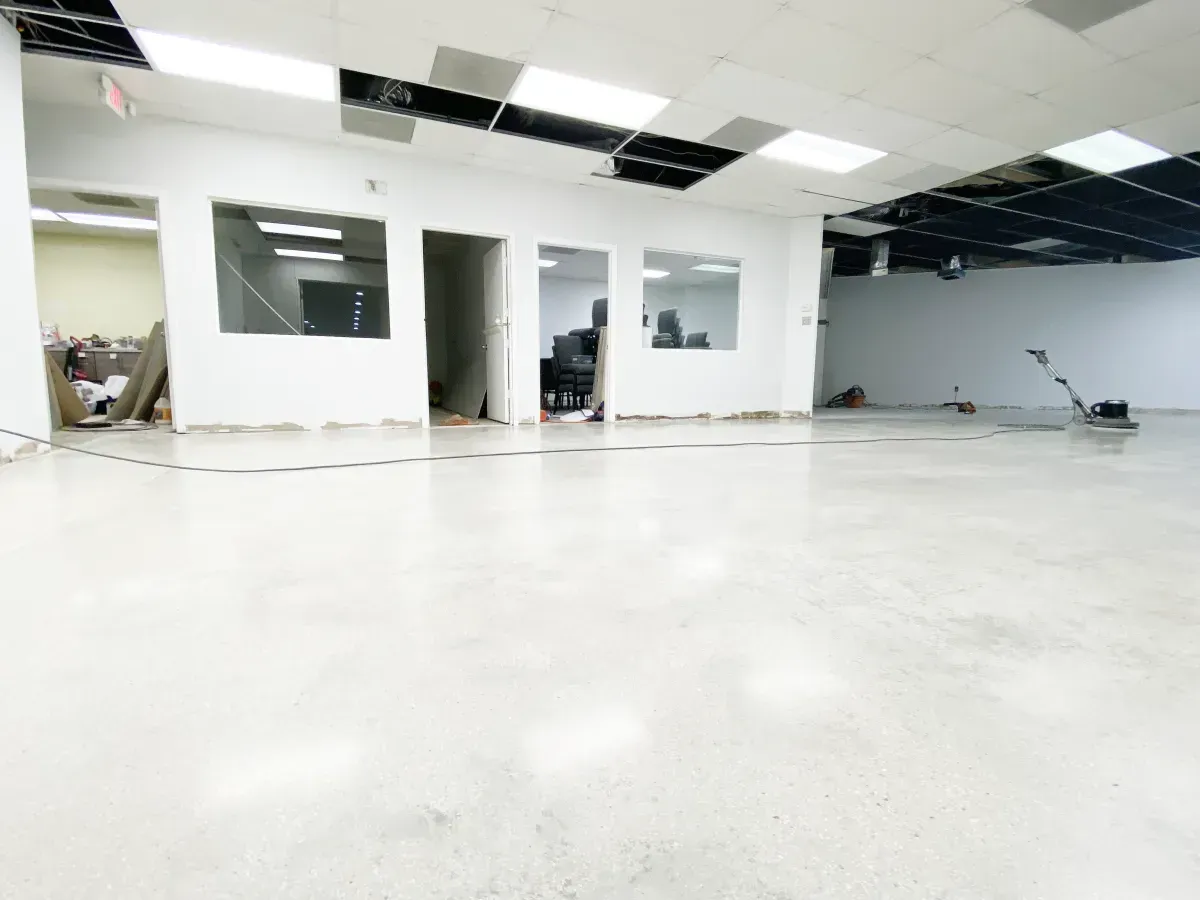 A spacious, modern office interior with polished white concrete floors, white walls, and a partially finished black ceiling.