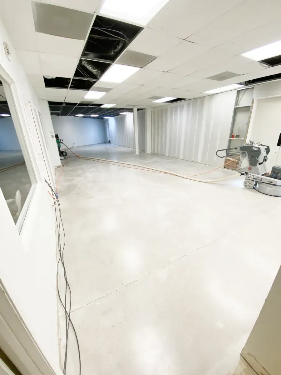 A wide-angle view of a bright, empty indoor commercial space featuring white walls, a concrete floor, and ceiling panels.